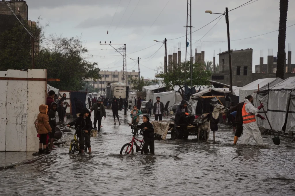 People walk through a flooded street lined with tents in Gaza.