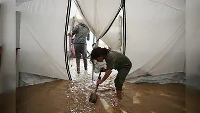 A child shovels muddy water from inside a flooded tent in Gaza.