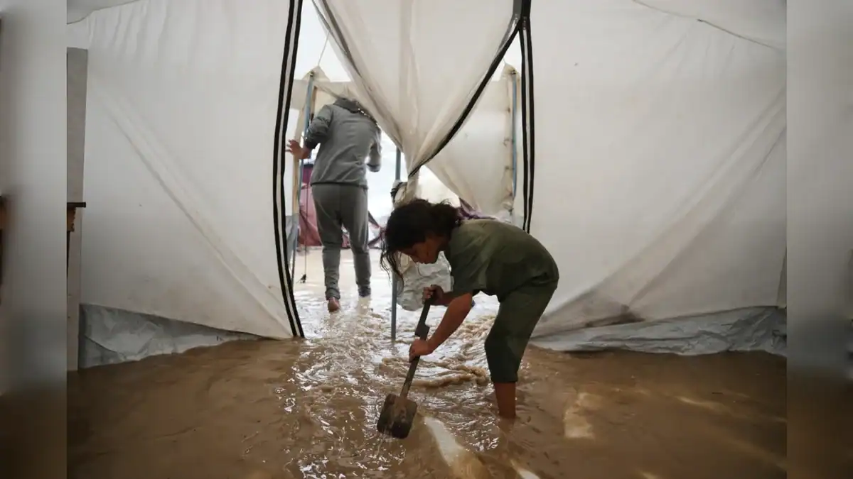 A child shovels muddy water from inside a flooded tent in Gaza.