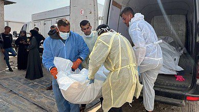 Health workers in protective suits carry a body bag from a vehicle after Israel handed over the bodies of Palestinians in Gaza.