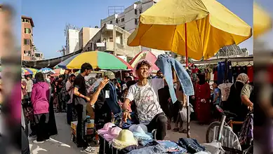 A young vendor holds up trousers at a crowded outdoor market in Gaza City.