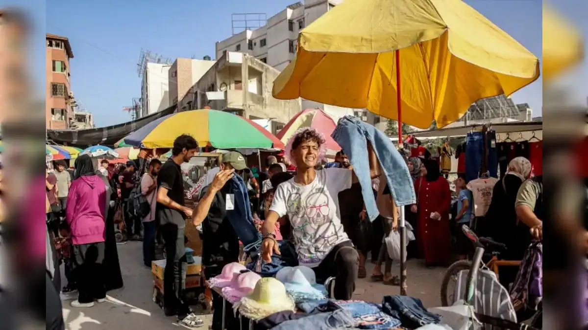 A young vendor holds up trousers at a crowded outdoor market in Gaza City.