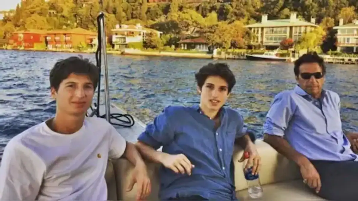 Three men seated on a boat with water and houses in the background.