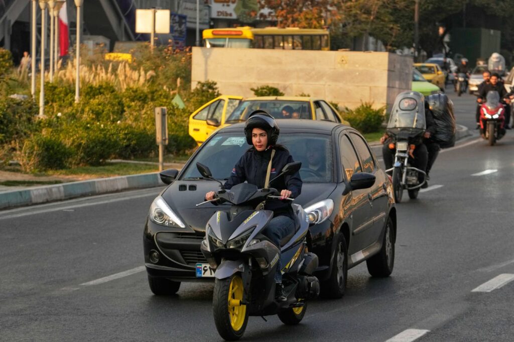 A woman rides a black motorbike along a busy street in downtown Tehran, Iran.
