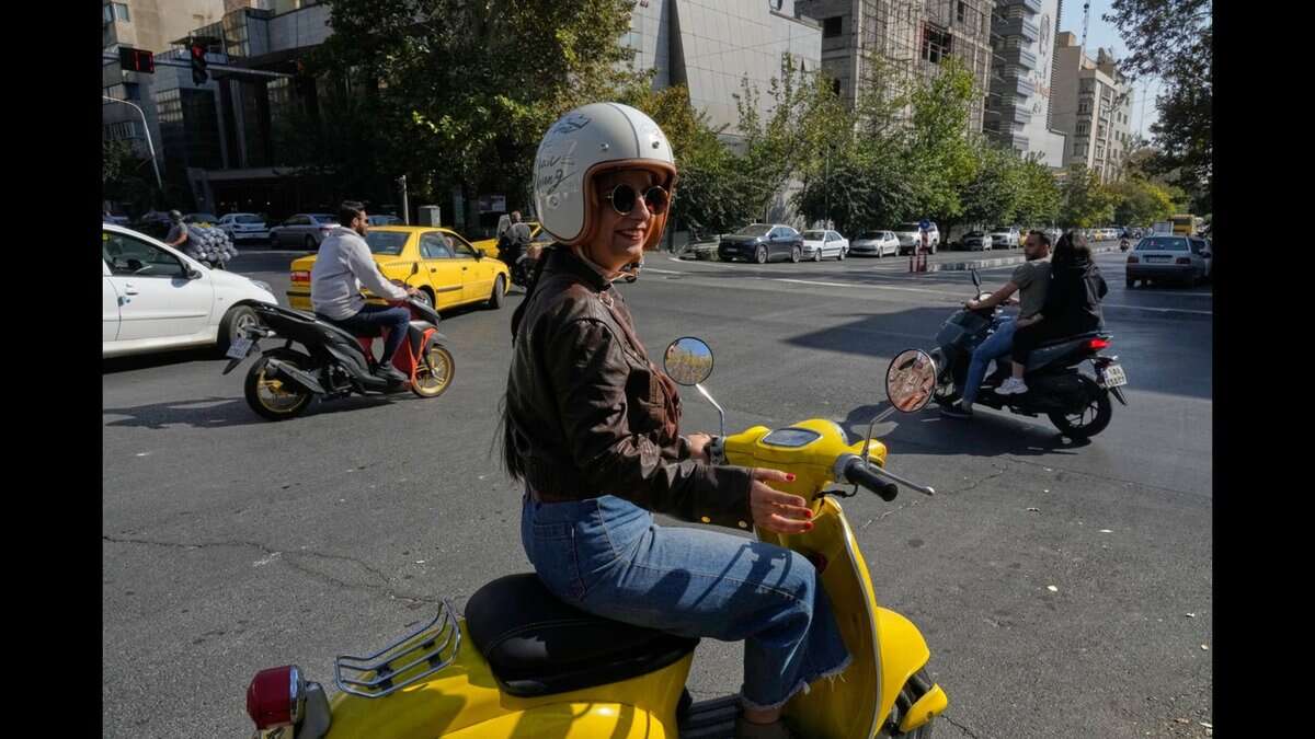 A woman rides a yellow scooter through a busy intersection in downtown Tehran, Iran.
