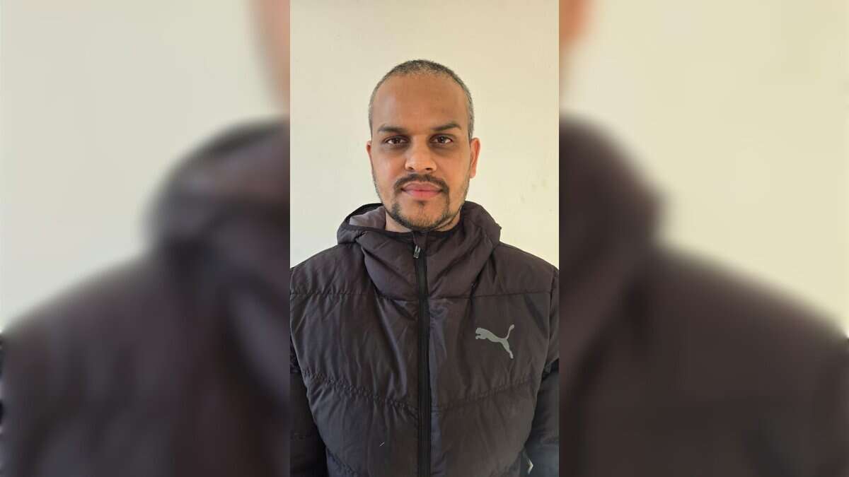 A man in a black winter jacket standing against a light-coloured wall.