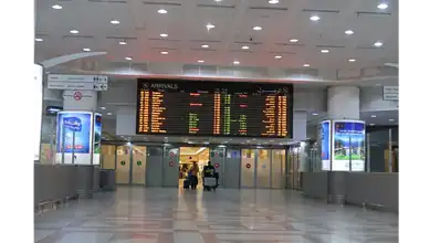 Passengers walk through the arrivals hall at Kuwait International Airport, where the digital board displays updated flight information.