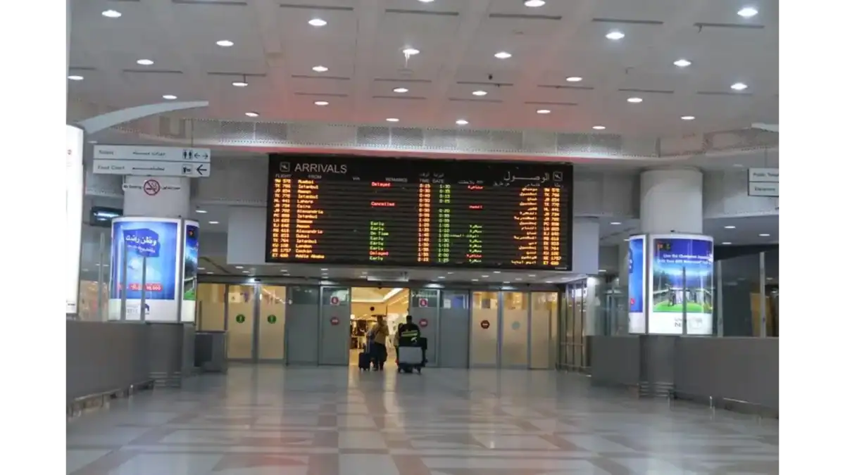 Passengers walk through the arrivals hall at Kuwait International Airport, where the digital board displays updated flight information.