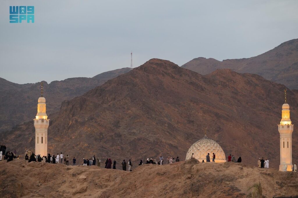 Visitors walking near the illuminated minarets and domed landmark at Mount Uhud in Madinah city.
