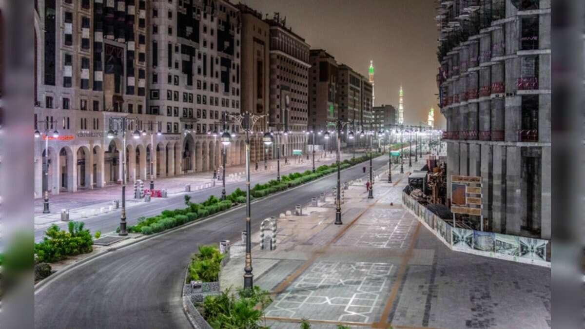 A quiet, well-lit street in Madinah at night with modern buildings and the Prophet’s Mosque minarets glowing in the distance.
