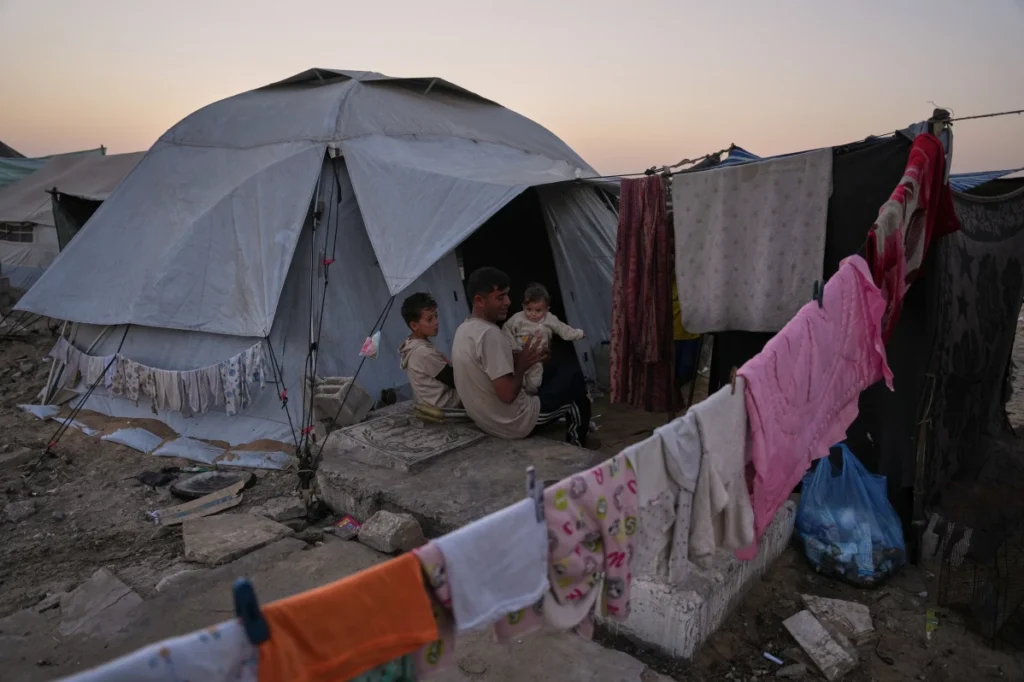 Mohammed Barabakh sits on a grave with his children beside their tent in a cemetery in Khan Younis, southern Gaza Strip.