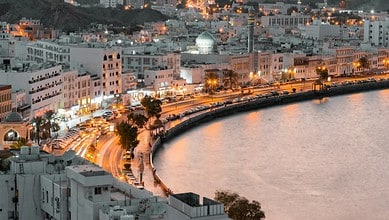 A scenic evening view of Muttrah Corniche in Muscat, Oman, with city lights reflecting on the waterfront.
