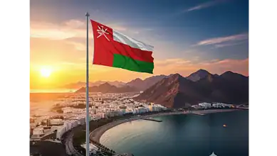 Omani flag waving over Muscat city at sunset with mountains in the background.