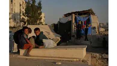 Palestinian children sitting on a grave near makeshift tents in a Khan Younis cemetery, southern Gaza Strip.