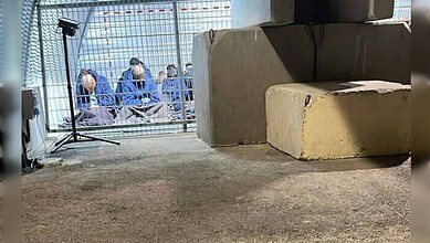 A group of blindfolded Palestinian detainees seated on the ground inside a fenced enclosure at the Sde Teiman military base, photographed under artificial lighting.