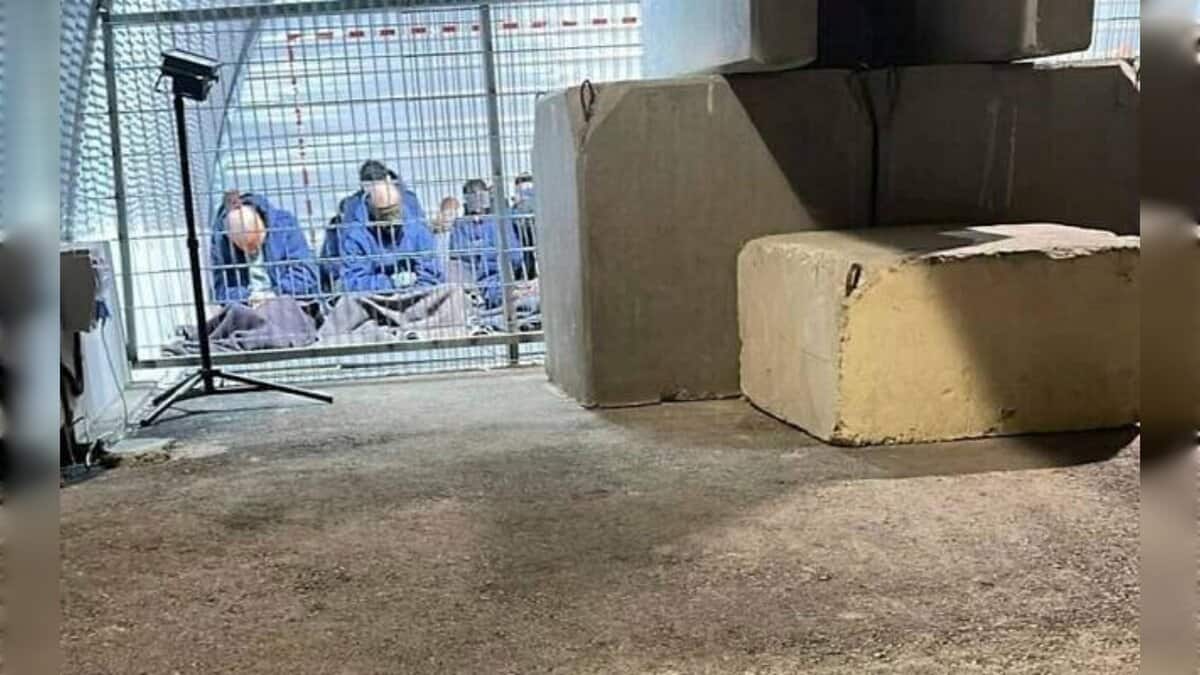 A group of blindfolded Palestinian detainees seated on the ground inside a fenced enclosure at the Sde Teiman military base, photographed under artificial lighting.