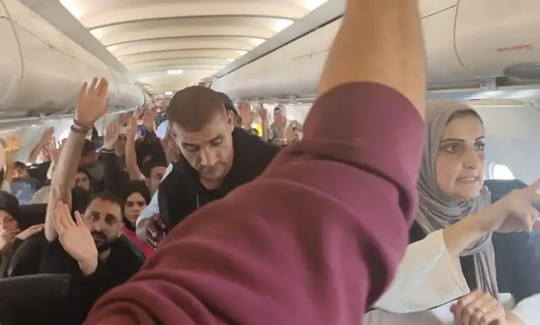 Passengers crowded inside an aeroplane cabin, raising their hands during a tense moment on board.