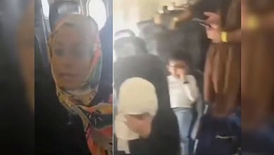 Passengers sit inside a crowded aircraft, with women and children visibly distressed during prolonged delay.