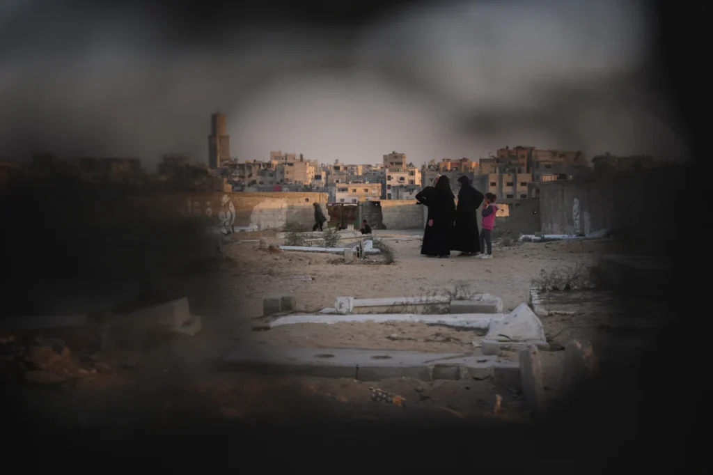 Palestinian women and a child stand among graves in a Khan Younis cemetery where displaced families have set up tents.