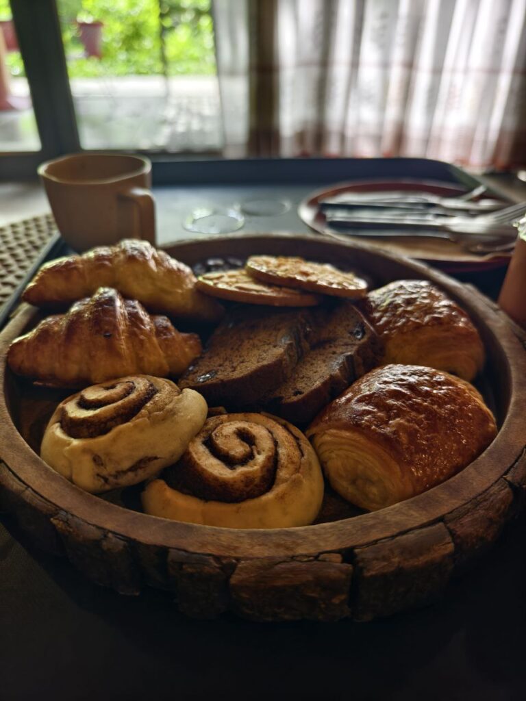 Delicious pastries including cinnamon rolls, croissants, and bread slices arranged in a wooden tray.