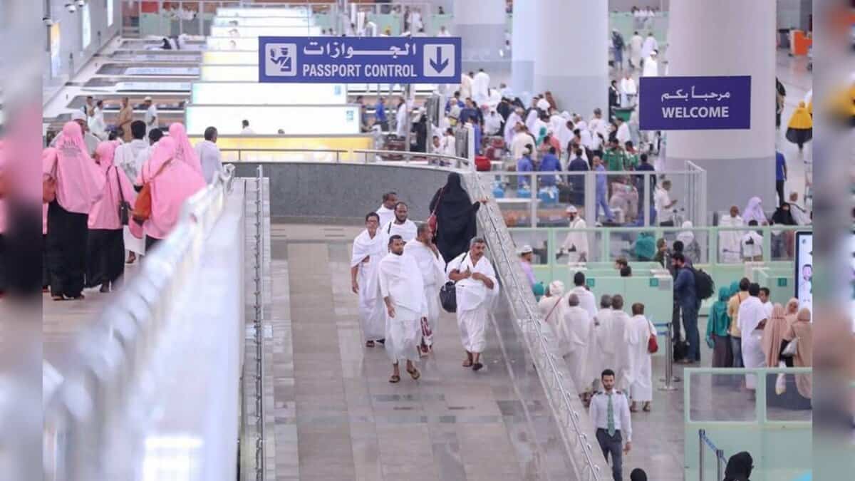 Pilgrims walking through a busy airport passport control area during Haj arrivals.