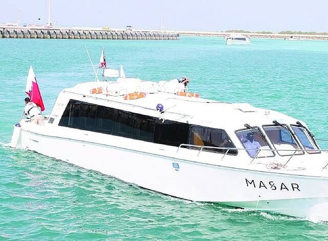 A white passenger ferry named MASAR, carrying the Qatari flag, sails through turquoise waters at Al Ruwais Port in Qatar.