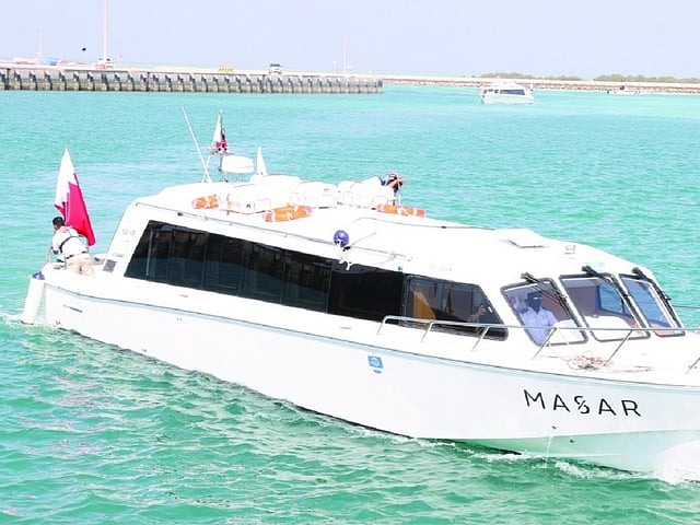A white passenger ferry named MASAR, carrying the Qatari flag, sails through turquoise waters at Al Ruwais Port in Qatar.