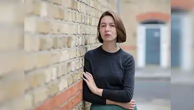 Irish author Sally Rooney standing against a brick wall.