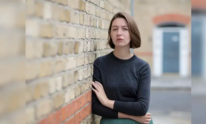 Irish author Sally Rooney standing against a brick wall.
