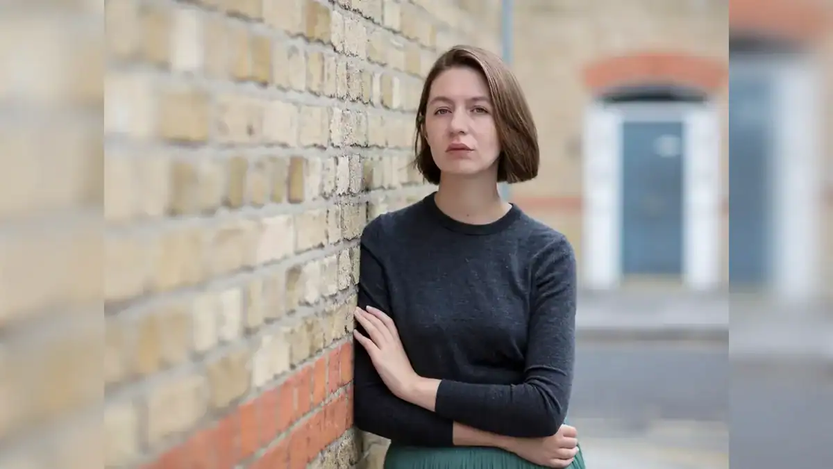 Irish author Sally Rooney standing against a brick wall.