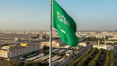 Saudi Arabian national flag flying high over a cityscape in Riyadh.