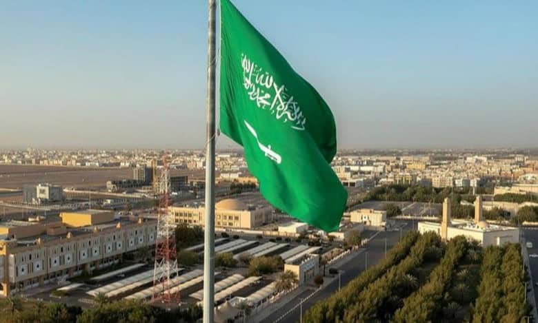 Saudi Arabian national flag flying high over a cityscape in Riyadh.
