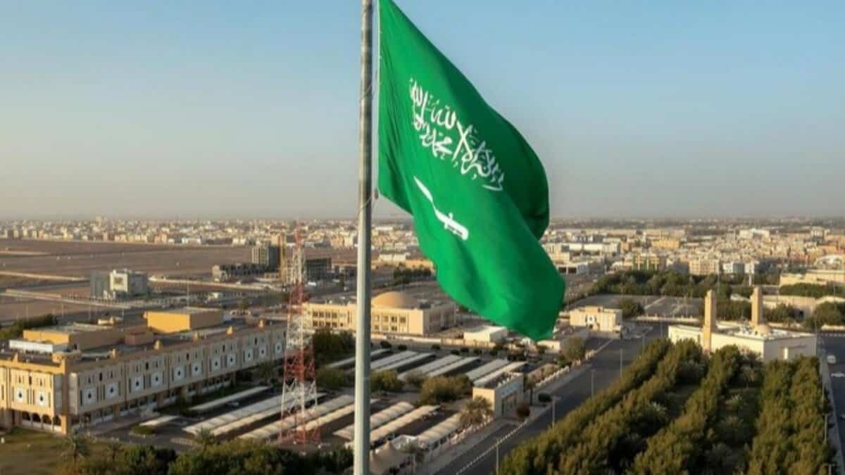 Saudi Arabian national flag flying high over a cityscape in Riyadh.