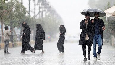 People walk through heavy rain in Saudi Arabia, some using umbrellas while others cross the street in wet conditions.
