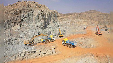 Aerial view of heavy machinery and trucks operating at a mining site in a rocky desert area in Saudi Arabia