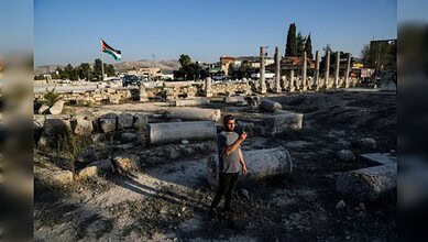 A man stands among Roman ruins in Sebastia as a Palestinian flag flies in the background.