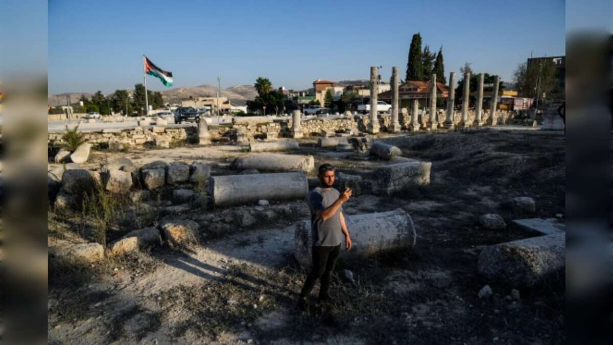 A man stands among Roman ruins in Sebastia as a Palestinian flag flies in the background.