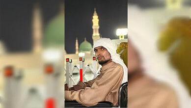 A man seated in a wheelchair in the courtyard of the Prophet’s Mosque in Madinah at night, with illuminated minarets in the background.