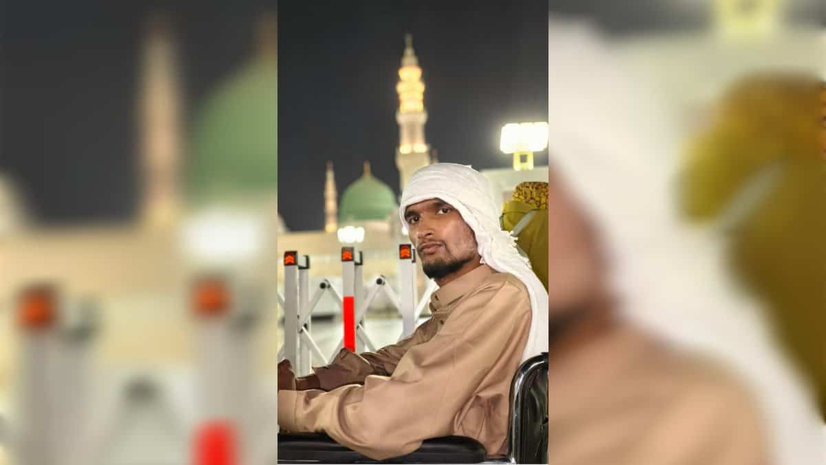 A man seated in a wheelchair in the courtyard of the Prophet’s Mosque in Madinah at night, with illuminated minarets in the background.