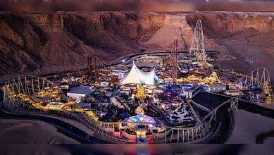 A night-time aerial view of Six Flags Qiddiya City, illuminated against the Tuwaiq Mountains with roller coasters and themed attractions.