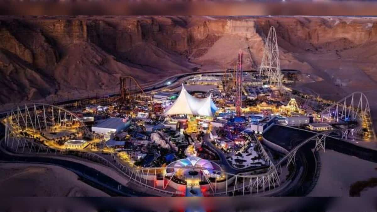 A night-time aerial view of Six Flags Qiddiya City, illuminated against the Tuwaiq Mountains with roller coasters and themed attractions.