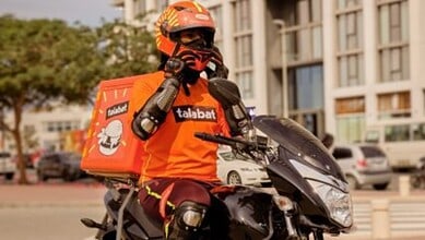 A delivery rider wearing protective gear and a helmet sits on a motorcycle in the UAE.