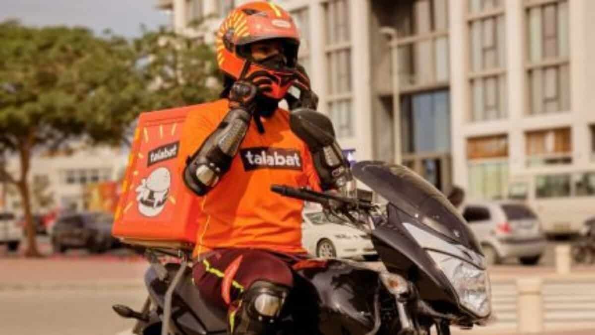 A delivery rider wearing protective gear and a helmet sits on a motorcycle in the UAE.