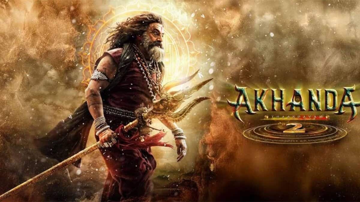 Movie poster for 'Akhanda 2' featuring a warrior with long hair and beard in traditional attire, holding a trident against a dramatic golden and dusty background with mystical circular symbols