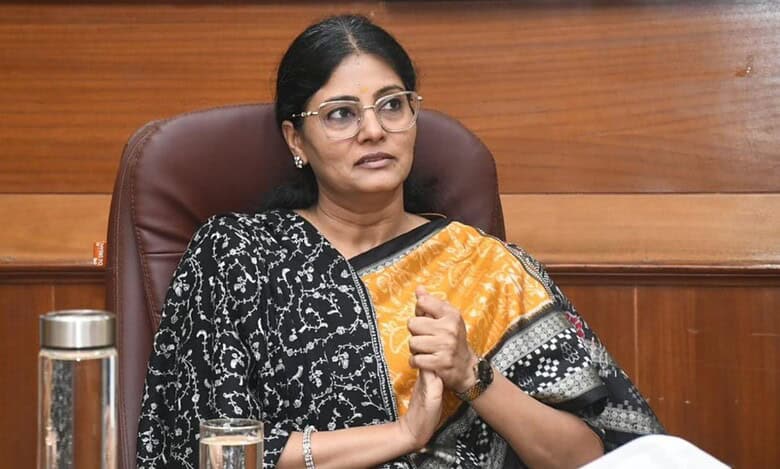 Anupriya Patel, Minister of State for Fertilisers, seated in an office chair wearing a black and orange patterned saree and glasses, with a water pitcher and glass on the desk