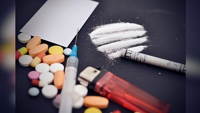 Image showing Assorted pills, a syringe, and lines of white powder with a rolled bill on a dark surface.
