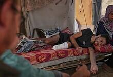 Yassin Marouf, 23, who lost his left foot and suffered a severe injury to his right leg after being hit by Israeli shelling in May, lies in a tent surrounded by his family in Zawaida, central Gaza (Abdel Kareem Hana/AP)
