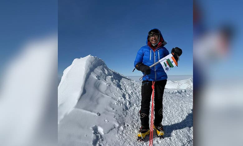 Mountain climber holding Indian flag on snowy summit ridge