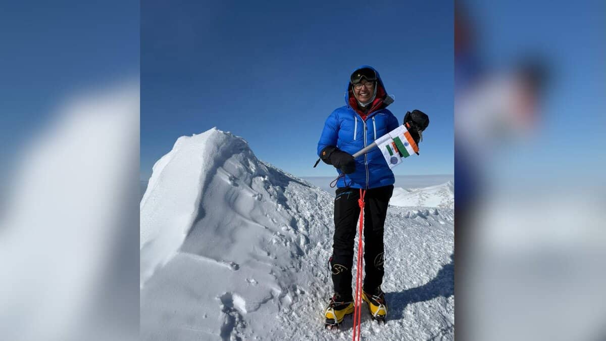 Mountain climber holding Indian flag on snowy summit ridge