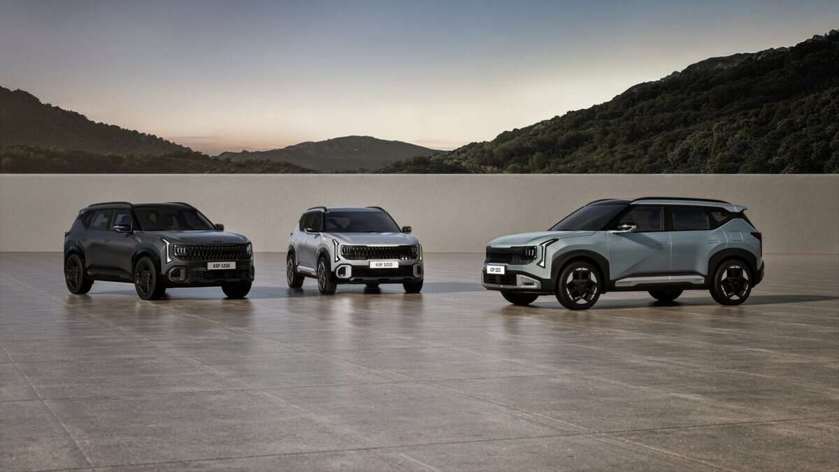 Three modern SUVs in dark gray, white, and light blue are displayed on a flat surface with rolling hills in the background at dusk.